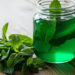 xarope de hortelã em uma jarra de vidro com folhas frescas de hortelã ao lado.