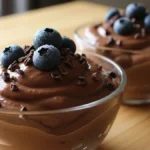 Mousse Cremosa de Abacate e Cacau - Duas taças de mousse cremosa de abacate e cacau com nibs e frutas vermelhas.